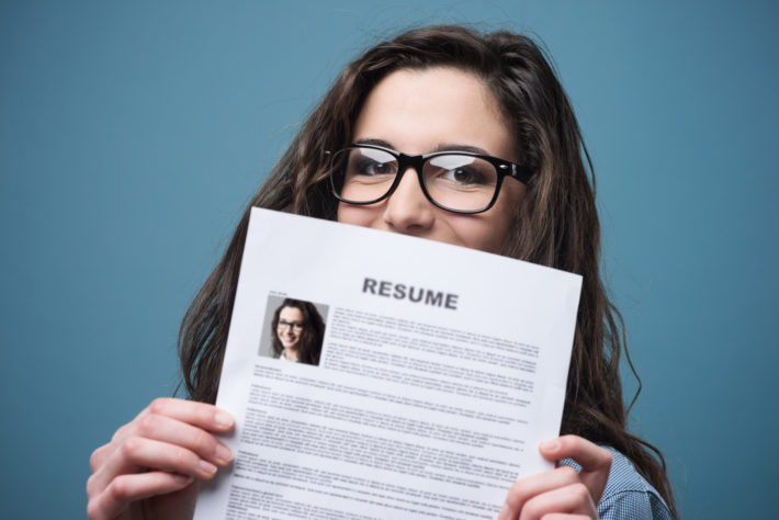 Young woman holds resume up in front of her face