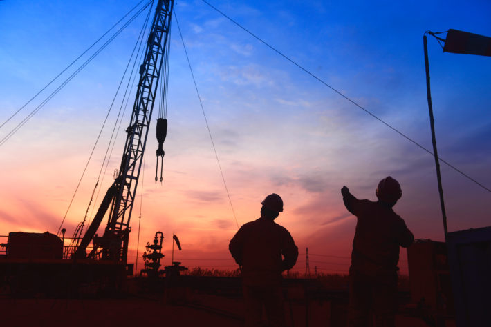 oil field workers stand around equipment in the field at sunset