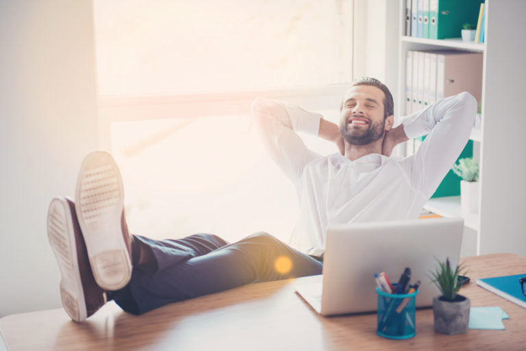 A business leader relaxes at his desk with a smile on his face
