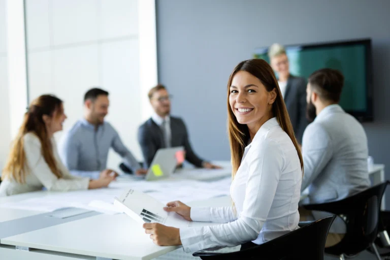 Woman smiling at camera as she sits at table with colleagues.